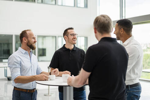 Eine Gruppe von Geschäftsleuten, die eine lockere Besprechung haben, während sie im Büroflur stehen und Tassen mit Kaffee halten - DIGF20378