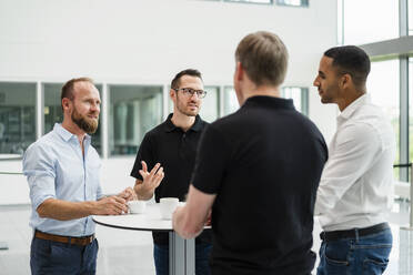 Group of businessman having informal meeting standing in office hall with cups of coffee - DIGF20379