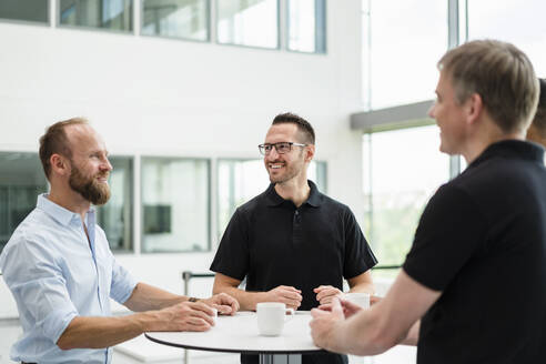 Eine Gruppe von Geschäftsleuten, die eine lockere Besprechung haben, während sie im Büroflur stehen und Tassen mit Kaffee halten - DIGF20380