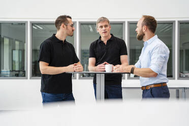 Group of businessman having informal meeting standing in office hall with cups of coffee - DIGF20381