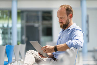 Businessman sitting in company auditory using digital tablet - DIGF20383