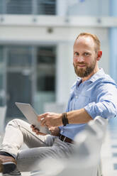 Businessman sitting in company auditory using digital tablet - DIGF20384