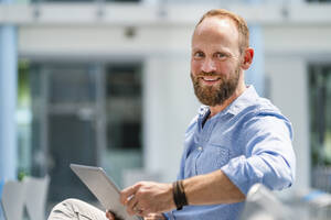 Ein Geschäftsmann sitzt in einem Hörsaal seines Unternehmens und benutzt ein digitales Tablet - DIGF20385