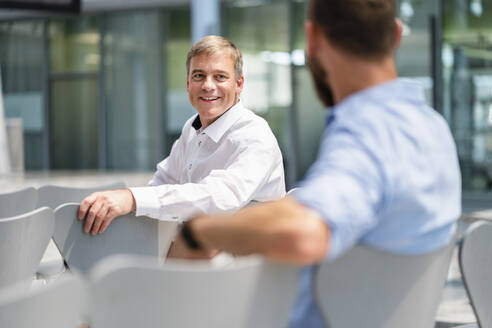 Selbstbewusster Geschäftsmann schüttelt einem Kollegen in einem Unternehmenssaal die Hand, bereit für eine produktive Besprechung - DIGF20391