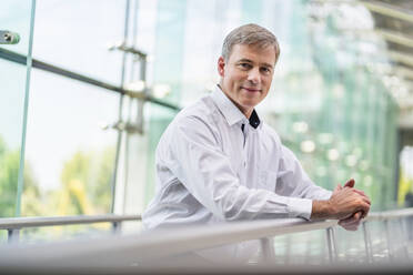 Confident businessman leaning on railing in office building - DIGF20402