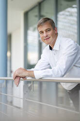 Serene businessman leaning on railing in office building - DIGF20414