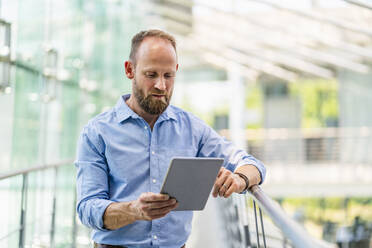 Ein erfahrener Geschäftsmann steht in einem Bürogebäude und nutzt ein digitales Tablet, um in Verbindung zu bleiben und produktiv zu arbeiten - DIGF20426