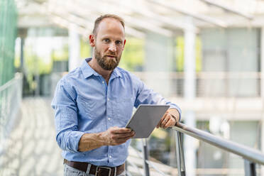 Ein erfahrener Geschäftsmann steht in einem Bürogebäude und benutzt ein digitales Tablet - DIGF20428