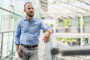 Serene businessman leaning on railing in office building - DIGF20429