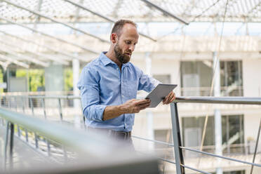 Ein erfolgreicher Unternehmer, der ein digitales Tablet benutzt, während er in einem Firmengebäude steht - DIGF20430