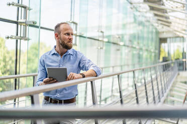 Ein erfahrener Unternehmer, der ein digitales Tablet benutzt, während er in einem Firmengebäude steht - DIGF20431