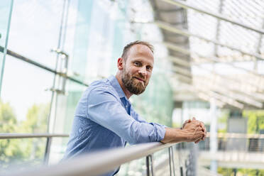 Confident businessman staning in office building leaning on railing - DIGF20433