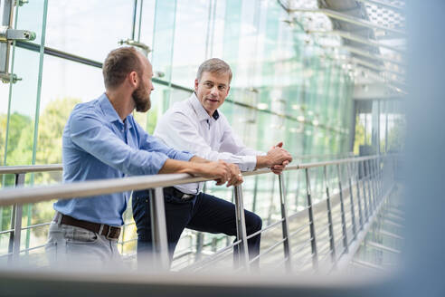 Colleagues talking in office building leaning on railing - DIGF20434