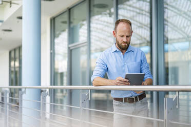 Ein erfahrener Unternehmer, der ein digitales Tablet benutzt, während er in einem Firmengebäude steht - DIGF20439