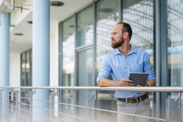 Ein erfahrener Unternehmer, der ein digitales Tablet benutzt, während er in einem Firmengebäude steht - DIGF20440