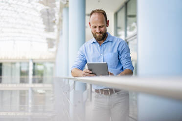 Ein erfahrener Geschäftsmann steht in einem Bürogebäude und benutzt ein digitales Tablet - DIGF20441