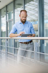 Experienced businessman using digital tablet standing in office building - DIGF20442