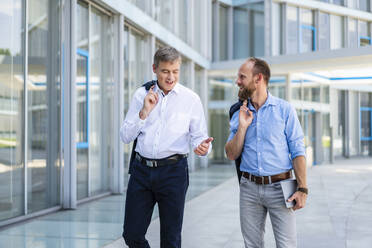 Zwei leitende Angestellte besprechen Geschäfte, während sie durch ein elegantes, modernes Bürogebäude schlendern - DIGF20449