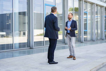 Two businessmen standing in front of office building talking - DIGF20466