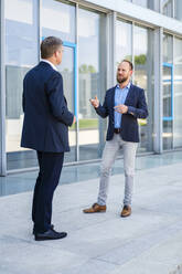 Two businessmen standing in front of office building talking - DIGF20467