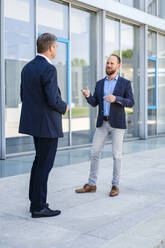 Zwei Führungskräfte eines Unternehmens im Gespräch vor einem modernen Bürokomplex - DIGF20467