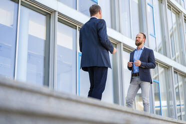 Zwei Führungskräfte unterhalten sich außerhalb ihres Arbeitsplatzes und diskutieren vor dem Bürogebäude über geschäftliche Angelegenheiten - DIGF20468