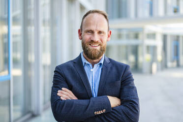 Confident businessman standing in office building with arms crossed - DIGF20472