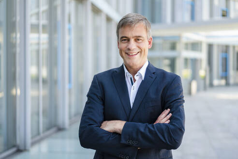 Confident businessman standing in office building with arms crossed - DIGF20475