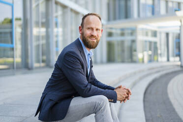 Serene businessman sitting in front of modern office building - DIGF20482