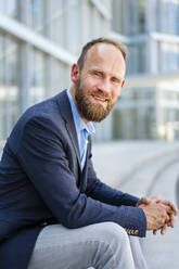 Serene businessman sitting in front of modern office building - DIGF20483