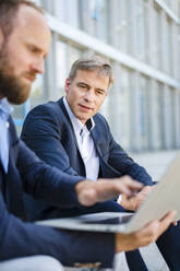 Two business colleagues sitting on steps working together on laptop - DIGF20488