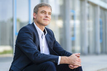 Serene businessman sitting in front of modern office building - DIGF20498