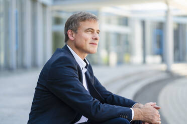 Serene businessman sitting in front of modern office building - DIGF20499