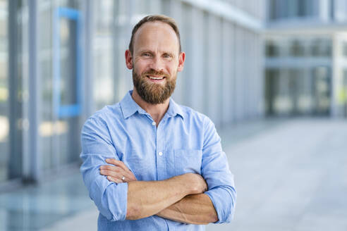 Casual businessman standing in front of office building with arms crossed - DIGF20507