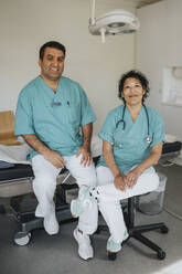 Portrait of smiling male and female doctors sitting in hospital - MASF37451