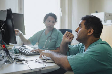 Male and female doctors discussing over computer at desk in hospital - MASF37457