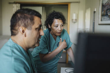 Male and female medical professionals discussing over computer in hospital - MASF37459