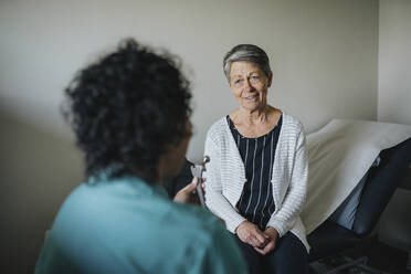 Doctor holding medical equipment discussing with patient in clinic - MASF37470