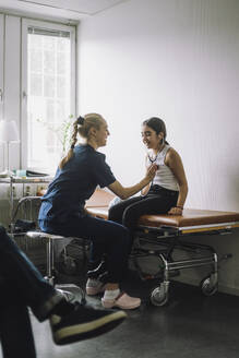 Female nurse examining girl sitting on bed in clinic - MASF37493