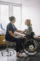 Female healthcare worker listening heartbeat of patient sitting on wheelchair in clinic - MASF37509