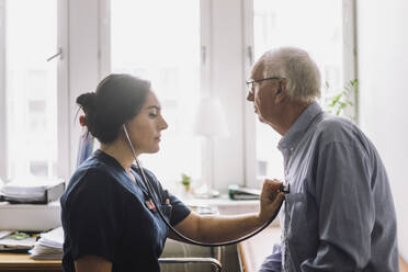 Side view of female nurse listening heartbeat of senior male patient in clinic - MASF37525