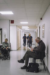 Side view of senior male patient sitting on chair in waiting room at hospital - MASF37555