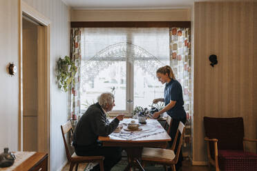 Älterer Mann im Gespräch mit weiblicher Pflegekraft beim Gießen von Pflanzen zu Hause - MASF37614