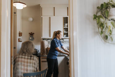 Side view of female care assistant working in kitchen at home - MASF37655