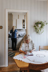 Senior woman solving puzzle while sitting on dining table at home - MASF37657