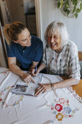 Happy senior woman solving puzzle while sitting with female care assistant at home - MASF37660