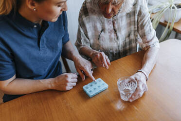 Hochformatige Ansicht einer weiblichen Pflegekraft, die einer älteren Frau zu Hause die Medikamentendosis erklärt - MASF37662