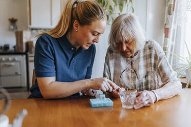 Weibliche Pflegekraft, die einer älteren Frau bei der Einnahme von Medikamenten zu Hause hilft - MASF37663