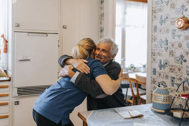 Lächelnder älterer Mann umarmt weibliche Betreuerin zu Hause - MASF37669
