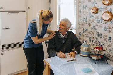 Female care assistant talking to senior man doing Soduko at home - MASF37670